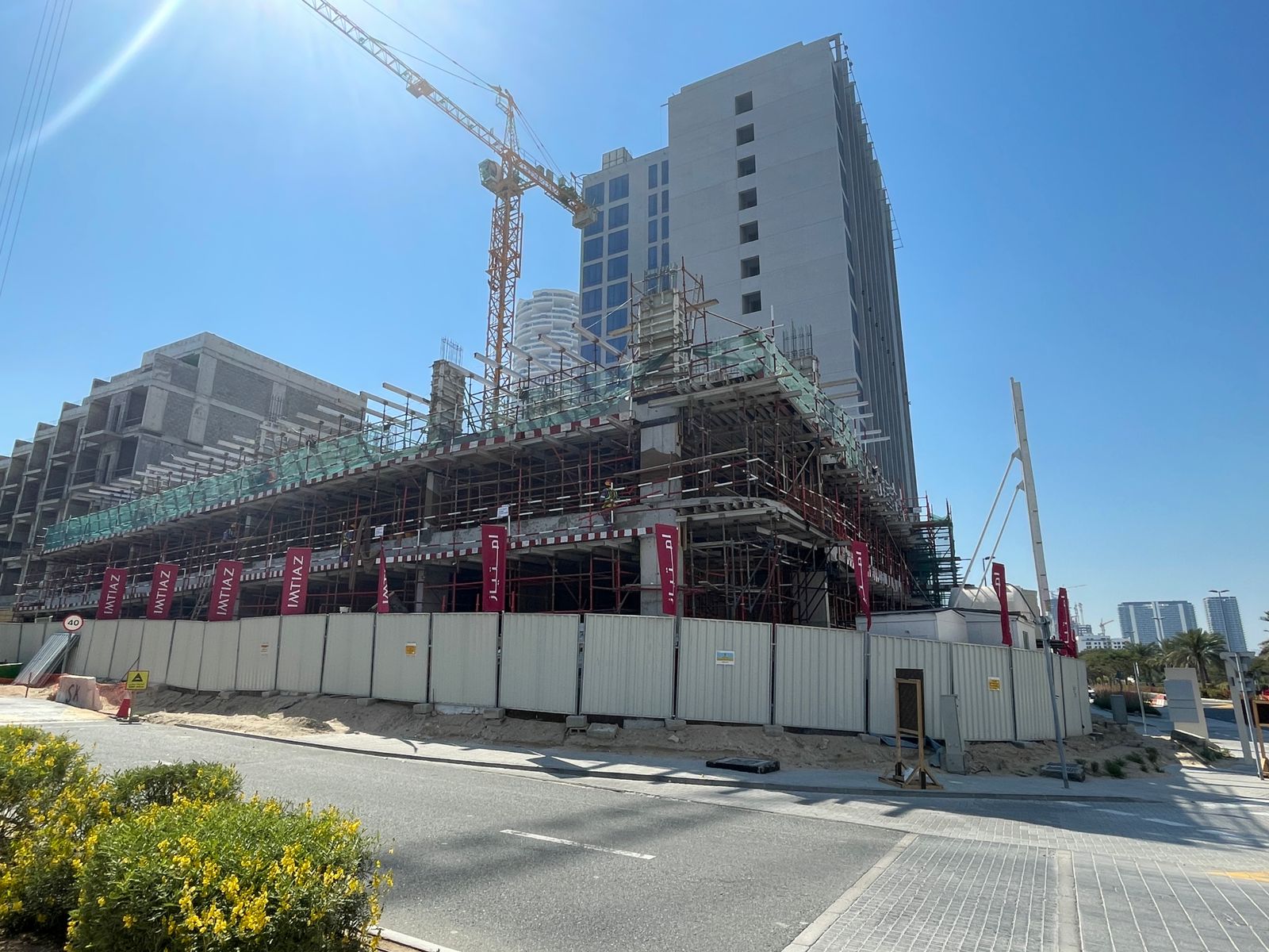 Pearl House By Imtiaz Construction site of a high-rise building with scaffolding, a crane, and nearby landscaping under a clear blue sky.